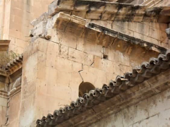 Figure 3. Photograph showing damage plainly visible from the exterior. The pinnacle on the end of the buttress and part of the cornice have collapsed. There is a crack over the arch located in the wall section of the buttress itself, and the keystone has dropped down. Plants can also be seen to be growing on the roof, an indicator of inadequate maintenance.